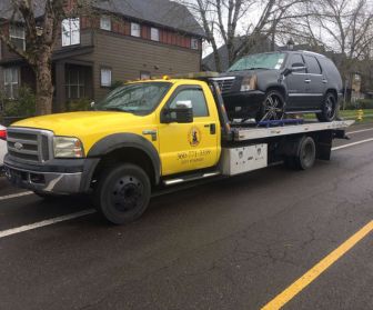 A yellow flatbed tow truck from Lucky Lab Towing LLC is parked on a residential street, transporting a black SUV, showcasing reliable urban towing and roadside assistance services.