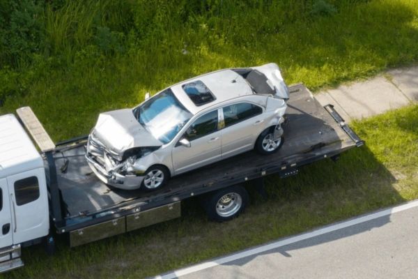 Accident towing services: A silver car with significant front damage being transported on a tow truck along the roadside.