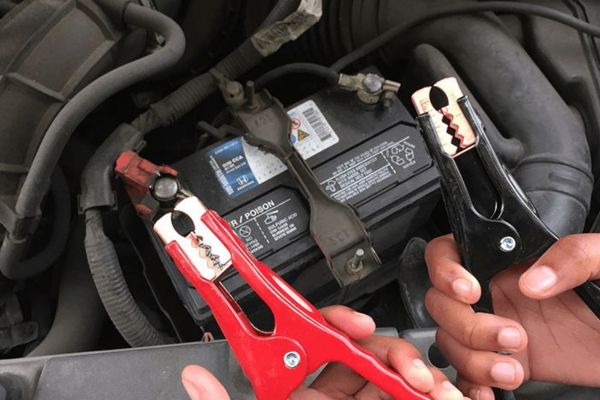 Hands holding red and black jumper cable clamps near a car battery terminal, showing the process involved in Jump Start Services to revive vehicles with dead batteries quickly and safely.