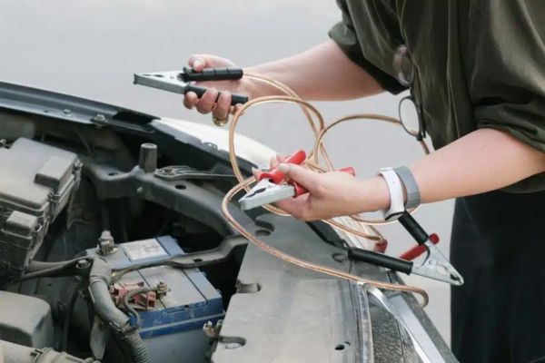A person prepares to connect jumper cables to a car battery under the hood, representing prompt and reliable Jump Start Services for vehicles with dead or drained batteries.