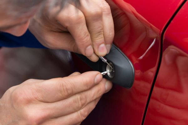 A close-up of a technician using lock-picking tools to unlock a red car door, highlighting the precision and urgency of Lockout Assistance Towing services for vehicle owners locked out of their cars.