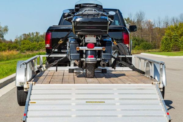 A black motorcycle is securely strapped onto a trailer hitched to a pickup truck on a sunny day, representing professional and safe Motorcycle Towing services for transport or roadside assistance needs.