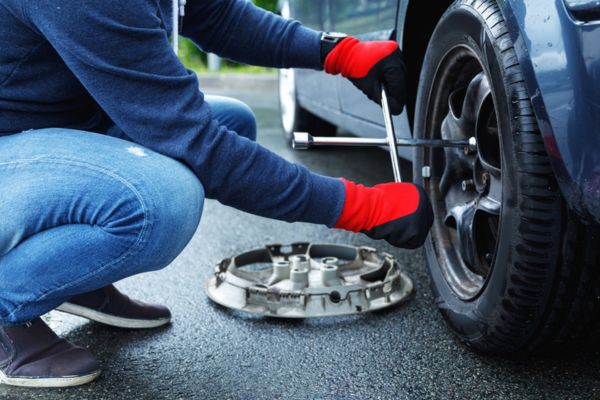 A person wearing red gloves uses a lug wrench to loosen bolts on a car wheel during a roadside tire replacement, exemplifying quick and efficient Tire Change Services for flat tire emergencies.