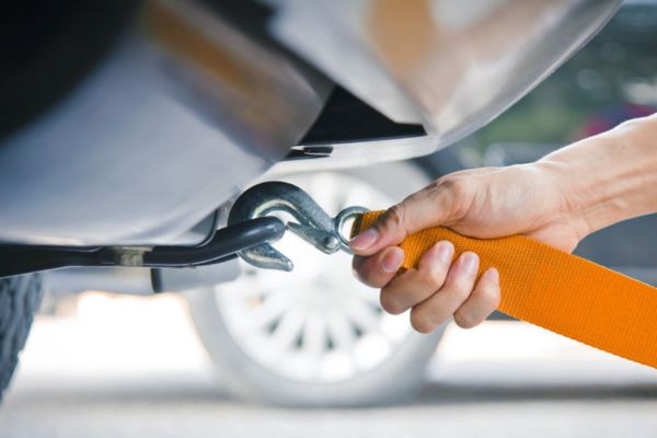 A close-up view of a person attaching a tow strap to a vehicle’s tow hook, illustrating the initial step in Winch Out Towing services for safely recovering a stuck or immobilized car.