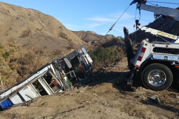 A heavy-duty tow truck uses a winch to recover a large commercial vehicle that has veered off-road into a ravine, demonstrating the strength and reliability of Winch Out Towing services in challenging terrain recovery situations.